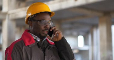 Afrikalı Amerikalı işçiler akıllı telefondan konuşur. İnşaat ustabaşı inşaat alanında duruyor ve cep telefonuyla konuşuyor.