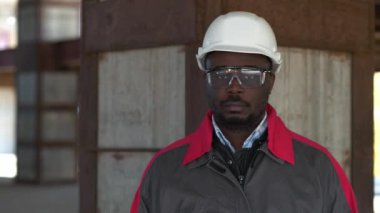 Beyaz şapkalı ve koruyucu gözlüklü Afrikalı Amerikalı işçiler inşaat alanında durup kameraya bakıyorlar.
