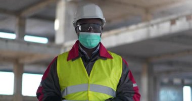 Tıbbi koruyucu maskeli Afrikalı Amerikalı işçiler inşaat alanında durup kameraya bakıyorlar.