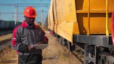 Yük treni istasyonundaki vagonların müfettişi tablet bilgisayarına not alır. Yük treni terminalinde tablet bilgisayarlı Afrikalı Amerikan demiryolu işçisi.