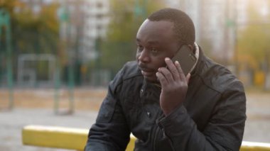 Slow Motion Afrikalı Amerikalı adam spor sahasında oturuyor ve akıllı telefondan konuşuyor.