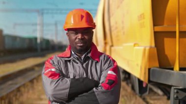 Afrikalı Amerikan demiryolu işçisi yük treni terminalinde duruyor. Demiryolu işçisi üniformalı ve kırmızı şapkalı, kameraya bak.