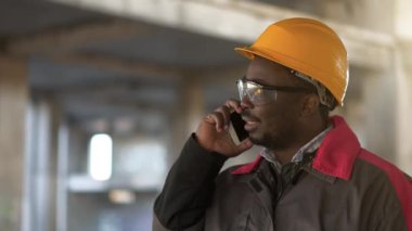 Afrikalı Amerikalı işçiler akıllı telefondan konuşur. Çalışmaların yöneticisi inşaat alanında duruyor ve cep telefonuyla konuşuyor