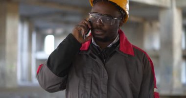 Afrikalı Amerikalı işçiler inşaat alanında akıllı telefondan konuşuyor. Başlıklı işçi proje sitesinde akıllı telefondan konuşuyor. Sinema 4K 60fps video
