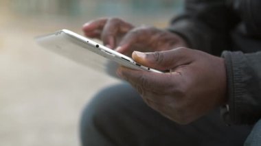 Slow Motion Afrikalı Amerikalı adam tablet bilgisayar kullanıyor. Siyah adamın elleri bir tablet bilgisayar tutuyor, yakın çekim. Tablet bilgisayarlı Afrikalı çalışmalar, sosyal ağlarda görüntülere göz atıyor
