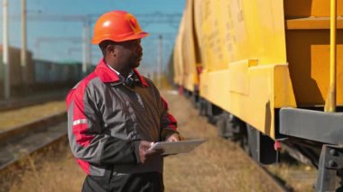 Yük treni terminalinde tablet bilgisayarı olan Afrika kökenli Amerikalı bir demiryolu işçisi. Tren istasyonundaki tren trafiği müfettişi tablet bilgisayarına not alır.