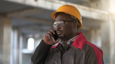 Afrikalı Amerikalı işçiler inşaat alanında akıllı telefondan konuşuyor. Sarı şapkalı mimar proje alanında akıllı telefondan konuşuyor.