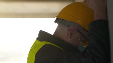 Slow Motion Stresli işçi ellerini duvara vuruyor. İnşaatçı inşaat alanında duruyor ve kafasını duvara vuruyor. Kendini kınama, kendine işkence, endüstriyel kaza.