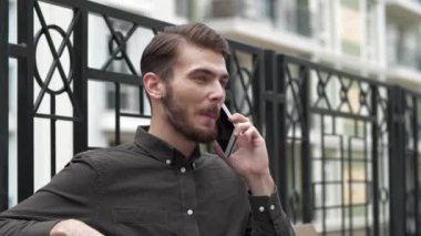 Genç yakışıklı işadamı bankta oturur ve akıllı telefonda konuşur.