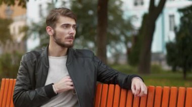 Siyah deri ceketli genç yakışıklı adam cebinden bir maske çıkardı ve onu giydi. Covid konsepti sağlık ve güvenlik, koronavirüs karantinası, sosyal mesafe. 4K Yavaş Hareket videosu
