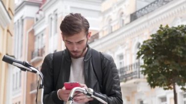 Genç yakışıklı adam bisikletiyle caddede duruyor ve akıllı telefondan bakıyor. Sonra iyi haberleri okudu ve şiddet dolu duygular, neşe ve neşe aldı.