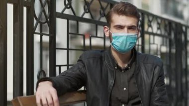 Tıbbi koruyucu maskeli yakışıklı adam bankta oturur ve kameraya bakar. Covid konsept sağlık ve güvenlik, koronavirüs karantinası, sosyal uzaklık, bir sonraki dalga covid virüs koruması