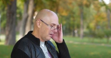 Gözlüklü yaşlı kel adam kendini iyi hissetmiyor ve başı ağrıyor. Kafasına masaj yapıyor. Sinema 4K 60fps video