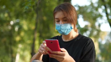 Koruyucu maskeli kız akıllı telefonundaki fotoğraflara bakıyor. Covid konsept sağlık ve güvenlik, koronavirüs karantinası, sosyal uzaklık, bir sonraki dalga covid virüs koruması