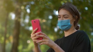 Slow Motion Genç kadın tıbbi koruyucu maskeli akıllı telefonla video bağlantısıyla iletişim kuruyor.