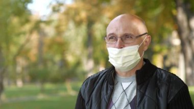 Tıbbi koruyucu maskeli ve gözlüklü kel bir adam badem yemiş.