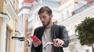 Genç adam bisikletle sokakta duruyor ve akıllı telefonuna bakıyor. Sonra iyi haberleri okudu ve şiddet dolu duygular, neşe ve neşe aldı.
