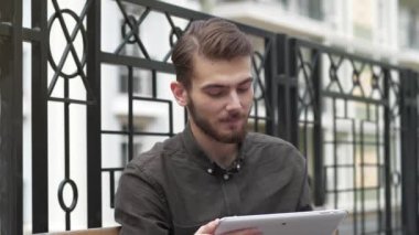 Slow Motion genç adam bankta oturuyor ve tablet bilgisayarla çalışıyor.
