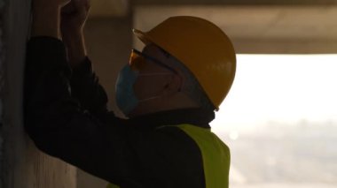 Slow Motion Workman ellerini ve kafasını duvara vuruyor. Stresli işçi inşaat alanında duruyor ve kafasını duvara vuruyor. Kendini kınama, endüstriyel kaza.