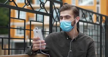 Yakışıklı genç adam, tıbbi koruyucu maskesini çıkardığından daha akıllı telefonuyla iletişim kuruyor. Gülümsüyor ve keyfi yerinde. Sinema 4K videosu