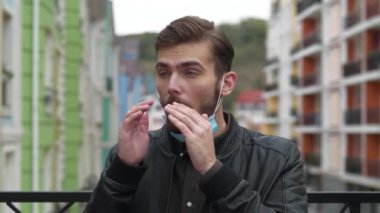 Ağır çekim genç hasta adam tıbbi koruyucu maskesini çıkarıp hapşırıyor ve burnunu siliyor. Sonra maskesini ve fermuarını taktı.