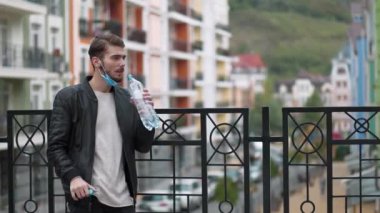 Genç adam koruyucu maskeyi çıkarıp şişeden maden suyu içiyor. 4K 60fps panoramik video