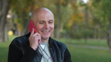 Şehir parkında gülümseyen son sınıf öğrencisi akıllı telefondan konuşuyor.