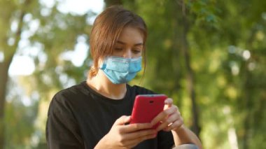 Tıbbi koruyucu maskeli genç bir kadın onun akıllı telefonuyla çalışıyor.