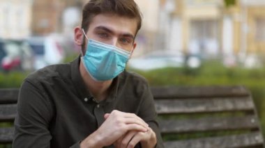 Tıbbi koruyucu maskeli bir öğrenci bankta oturur ve kameraya bakar. Covid konsept sağlık ve güvenlik, N1H1 koronavirüs karantinası, sosyal uzaklık, bir sonraki dalga covid virüs koruması