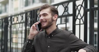 Genç adam bankta oturur ve akıllı telefonla konuşur, gülümser ve keyfi yerindedir.