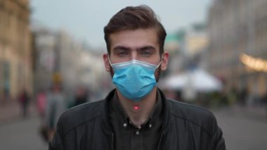 Tıbbi koruyucu maskeli genç adam sokakta dikiliyor ve kameraya bakıyor. Kırmızı lazer ışını yükselir ve alnında parlar, adam gözlerini kapar ve atışını bekler.