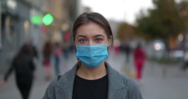 Mavi tıbbi koruyucu maskeli genç bir kadın sokakta duruyor. Covid konsept sağlık ve güvenlik, koronavirüs karantinası, sosyal uzaklık, bir sonraki dalga covid virüs koruması. Sinema 4K 60fps video