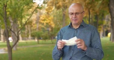 Gözlüklü kel yaşlı adam maskesini çıkardı, tekrar maskeyi taktı ve eline bir tablet bilgisayar aldı. Sinema 4K 60fps video