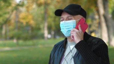 Siyah beyzbol şapkalı ve mavi koruyucu maskeli kıdemli adam akıllı telefondan konuşuyor. Covid konsept sağlık ve güvenlik, koronavirüs karantinası, sosyal uzaklık, bir sonraki dalga covid virüs koruması