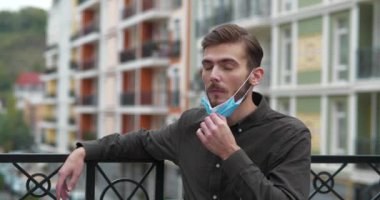 Genç adam tıbbi koruyucu maskeyi çıkarıp derin bir nefes alıyor. Maskenin içinde nefes alamıyor. Sinema 4K 60fps video