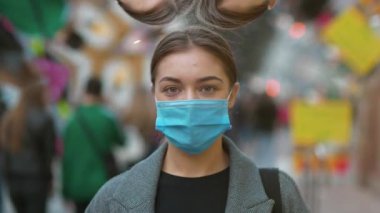 Kalabalık bir caddede tıbbi koruyucu maskeli genç bir kadın, gerçeği çarpıtan bir video ile kameraya bakıyor. Covid konsept sağlık ve güvenlik, sonraki dalga covid virüs koruması