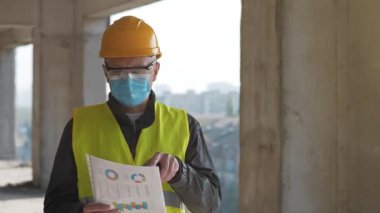 İnşaat alanında çalışan, kasketli ve tıbbi koruyucu maskeli işçiler, mali raporlarını elinde tutuyor ve taşınabilir radyo vericisiyle konuşuyor.