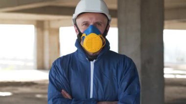 Solunum cihazında çalışan bir işçi, inşaat alanındaki koruyucu giysi ve şapka sana bakıyor.