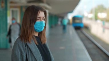 Mavi tıbbi koruyucu maskeli genç kadın metro istasyonunda duruyor.
