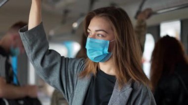 Metro vagonunda mavi tıbbi koruyucu maskeli genç bir kadın.