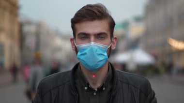 Mavi tıbbi koruyucu maskeli genç adam sokakta dikiliyor ve kameraya bakıyor. Kırmızı lazer ışını yükselir ve alnında parlar, adam gözlerini kapar ve alçakgönüllülükle atışını bekler.