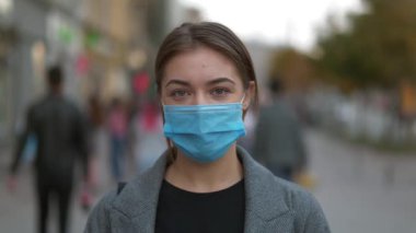 Kalabalık caddede mavi tıbbi koruyucu maskeli genç bir kadın. Covid konsept sağlık ve güvenlik, N1H1 koronavirüs karantinası, ikinci dalga covid virüs koruması. Zamanı Geri Alma Yavaş Hareket videosu
