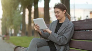 Slow Motion genç kız sonbahar şehir meydanında bankta oturuyor ve tablet bilgisayarındaki fotoğraflara bakıp duruyor.