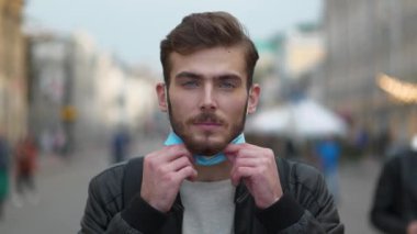 Genç adam tıbbi koruyucu maske takıyor, kalabalık bir caddede duruyor ve sana bakıyor. Covid konsept sağlık ve güvenlik, N1H1 koronavirüs karantinası