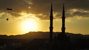 Ağır çekimde, gün batımında iki minareyle caminin yakınında uçan siyah kuzgunlar.