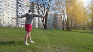 Adam şehir parkında çimenler üzerinde fiziksel egzersiz yapıyor.