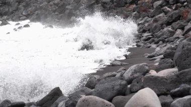 Ağır çekim, beyaz köpüklü dalgalar Tenerife, Kanarya Adaları, İspanya 'da siyah volkanik kumla sahilde kırılıyor.