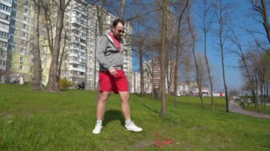 Bahçesinde spor lastiği olan komik bir adam. Adam parkta çimenler üzerinde fiziksel egzersiz yapıyor.