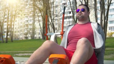 Sporcu bacaklar için yorucu bir egzersiz yapıyor. Adam spor sahasında fiziksel egzersiz yapıyor. Açık hava spor salonunda gözlüklü adam egzersizi yapıyor.