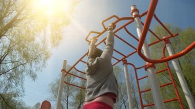 Adam spor sahasında fiziksel egzersiz yapıyor. Sporcu yorucu egzersizler yapıyor, barfiks çekiyor.